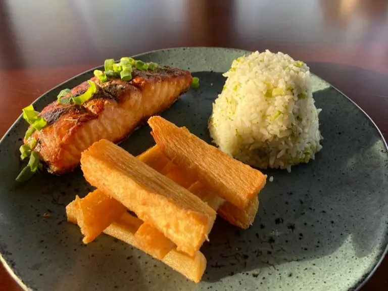 Prato de salmão grelhado servido com arroz branco e macaxeira frita crocante.